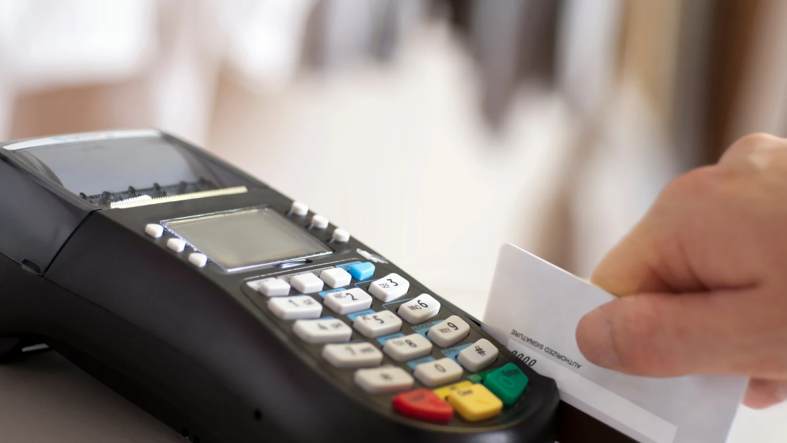 Mão inserindo um cartão de crédito na maquininha de pagamento sobre o balcão de uma loja